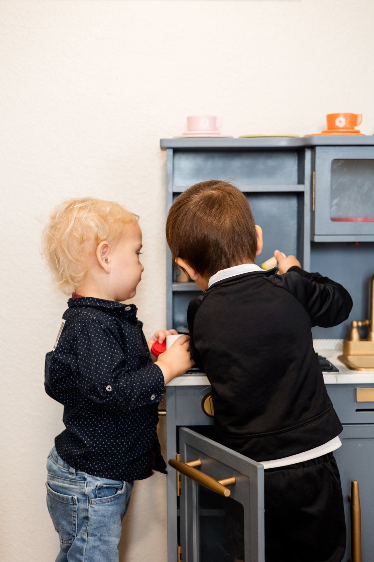Two toddlers playing together at a play kitchen.