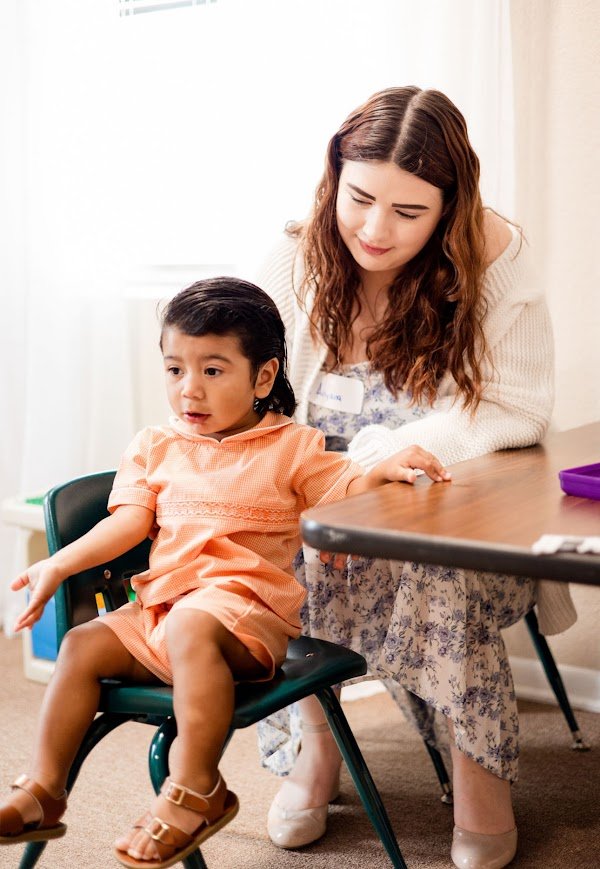 A volunteer helping a toddler at a table in children's ministry