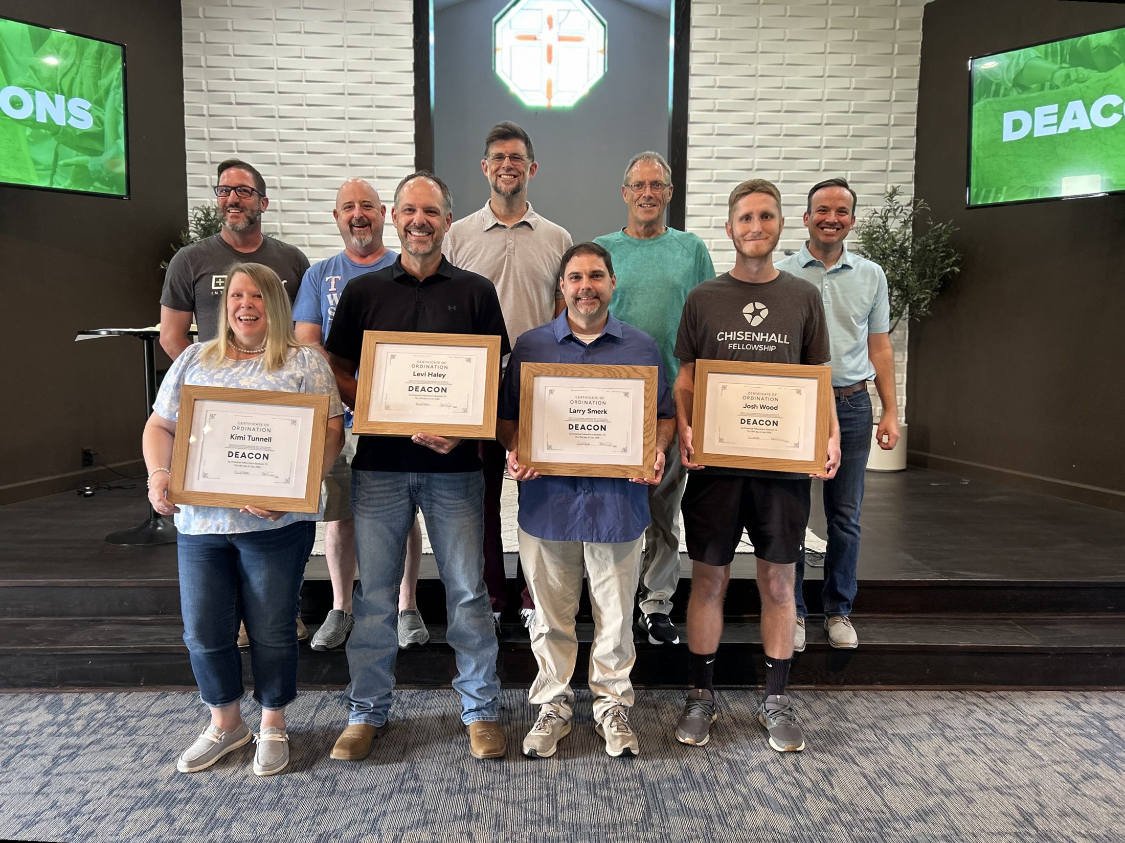 Pastors and deacons of Chisenhall Fellowship gathered on the stage, with four newly commissioned deacons in front, Kimi Tunnell, Levi Haley, Larry Smerk and Josh Wood, holding framed ordination certificates
